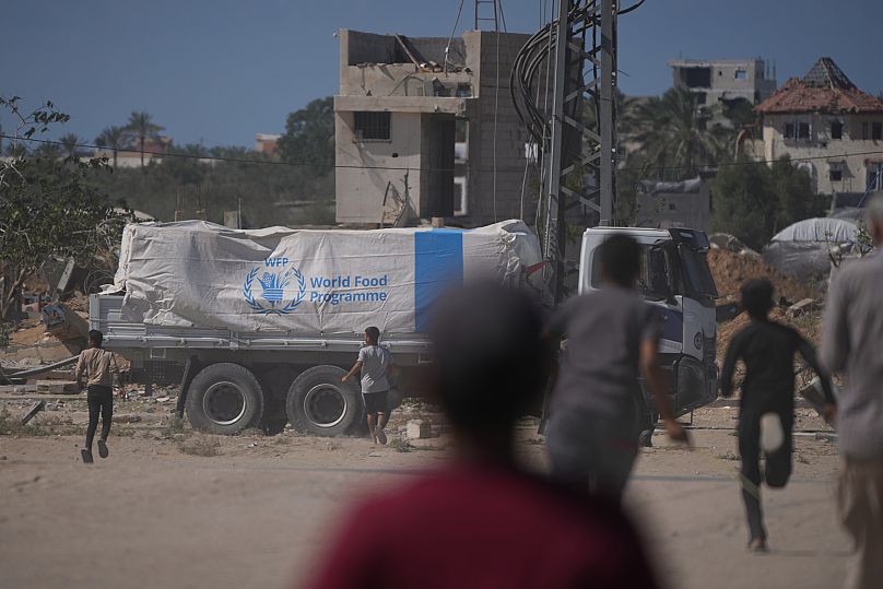 Os palestinianos correm para os camiões que transportam ajuda do Programa Alimentar Mundial enquanto passam por Deir al-Balah, 15 de outubro de 2025
