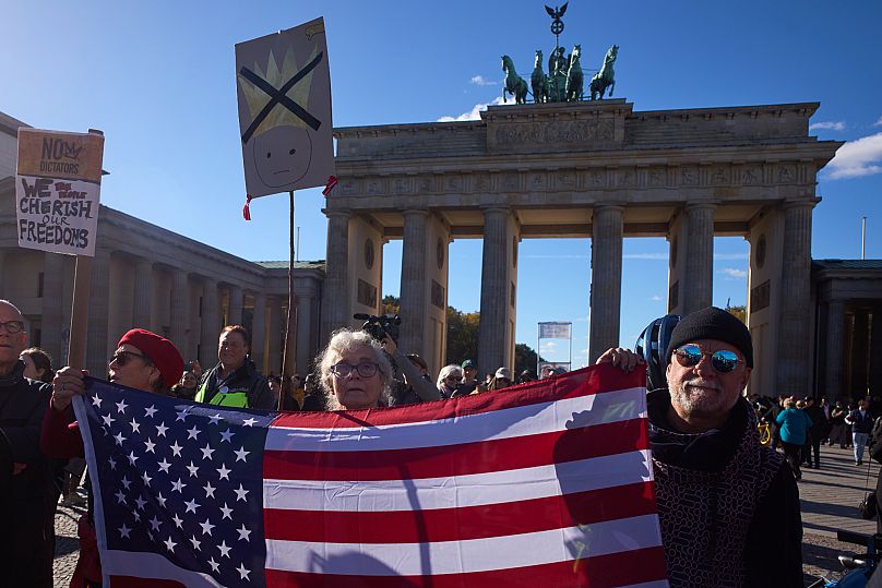 People display US flag and a "No Kings" sign as they participate in a pro-democracy, anti-Trump protest outside the US embassy in Berlin, Oct. 18, 2025.
