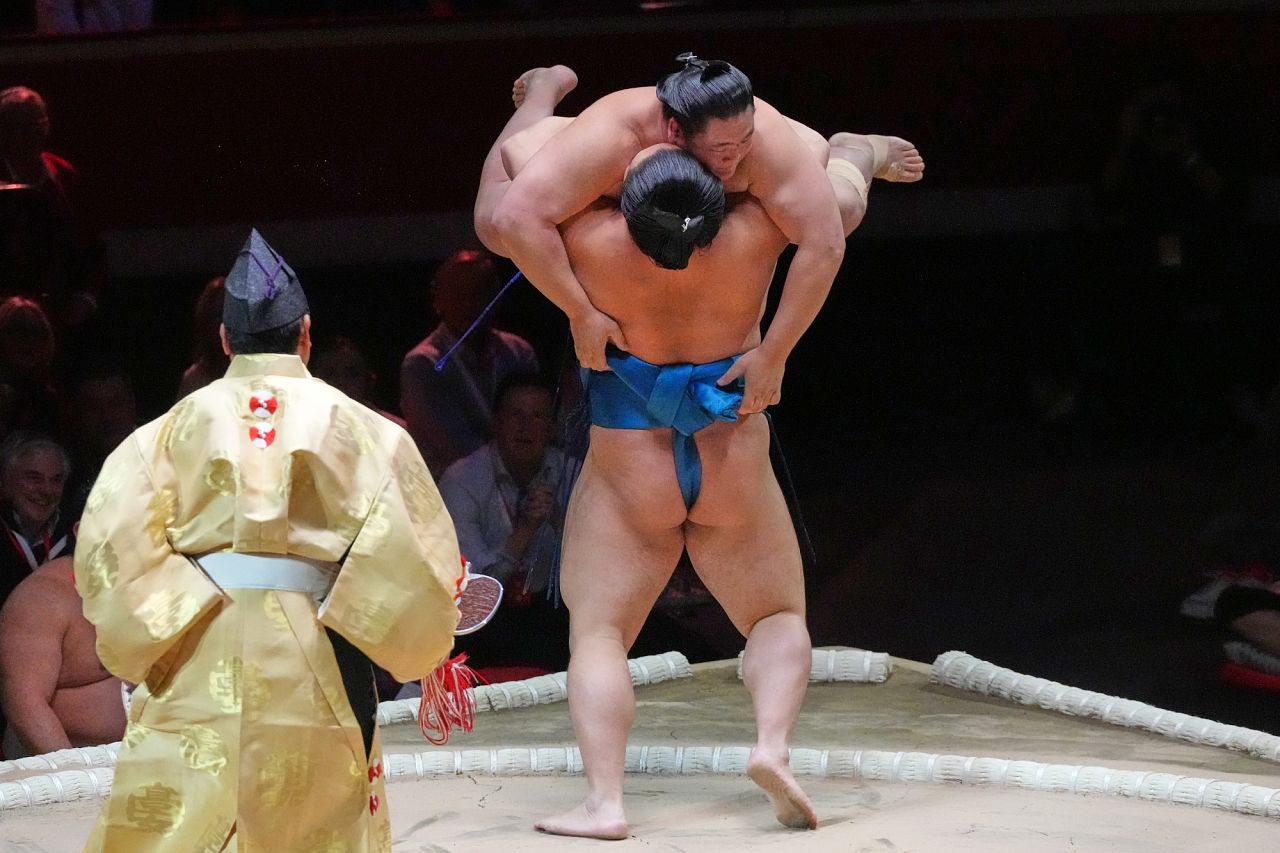 Kotoeiho, back to camera, pushes and lifts Oshoumi during their bout at The Grand Sumo Tournament. 