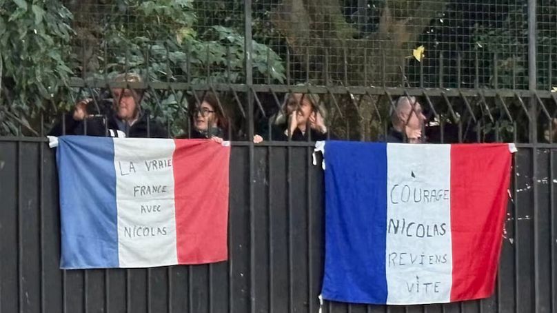Supporters show solidarity outside Nicolas Sarkozy's home, holding flags with inscriptions reading "Courage Nicolas, come back soon" and "True France with Nicolas"