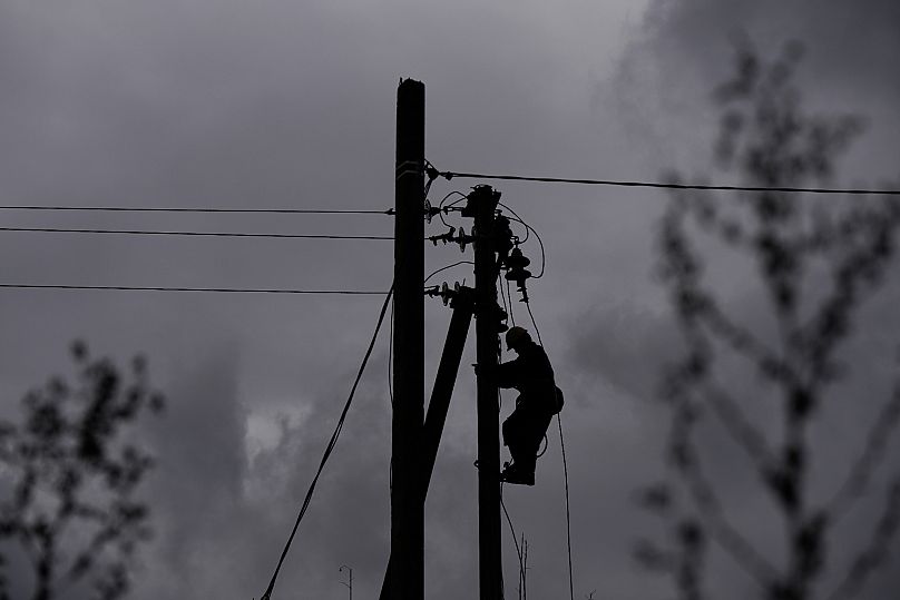 Un ouvrier grimpe sur un poteau électrique pour réparer les lignes endommagées lors d'une attaque russe à Shostka, le 16 octobre 2025.