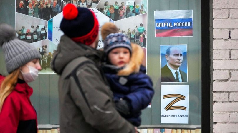 Eine Familie geht in St. Petersburg an einem Porträt des russischen Präsidenten, einem Schild mit der Aufschrift "Go Russia!" und dem Buchstaben Z vorbei