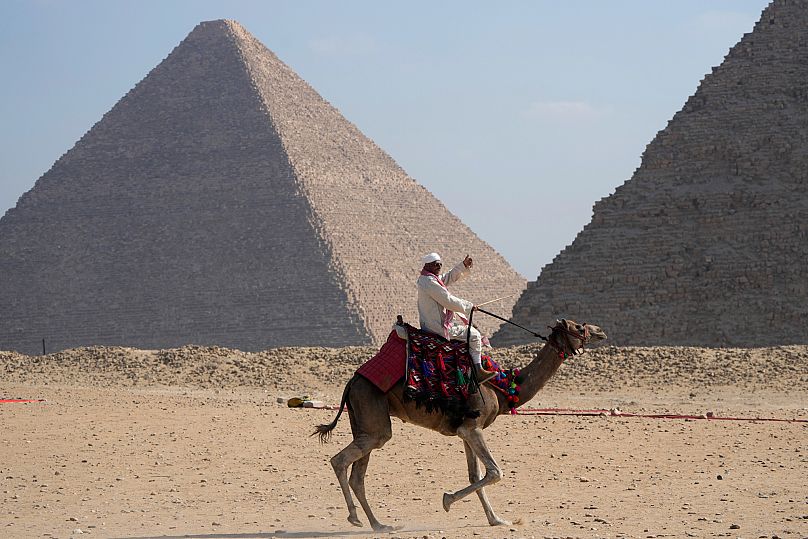 A tourist guide rides a camel at the historical site of Giza Pyramids, 29 October, 2024