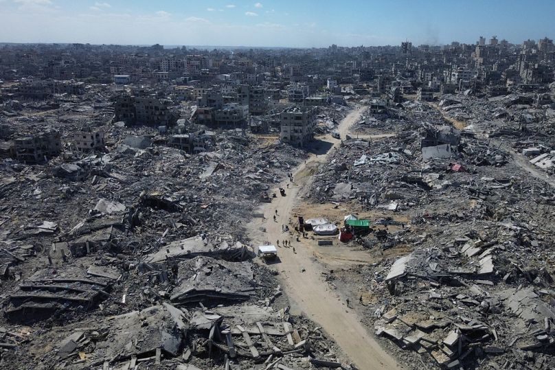 يسير فلسطينيون على طول شارع محاط بالمباني المدمرة خلال عامين من قصف الجيش الإسرائيلي في مدينة غزة، الأربعاء 15 أكتوبر/تشرين الأول 2025.