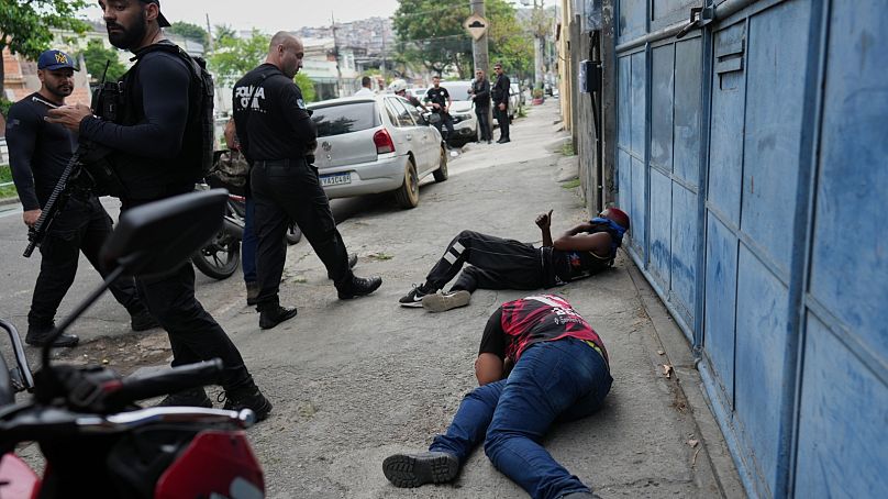 Rendőrök állnak a földön fekvő gyanúsítottak mellett a riói Complexo do Alemao favelában